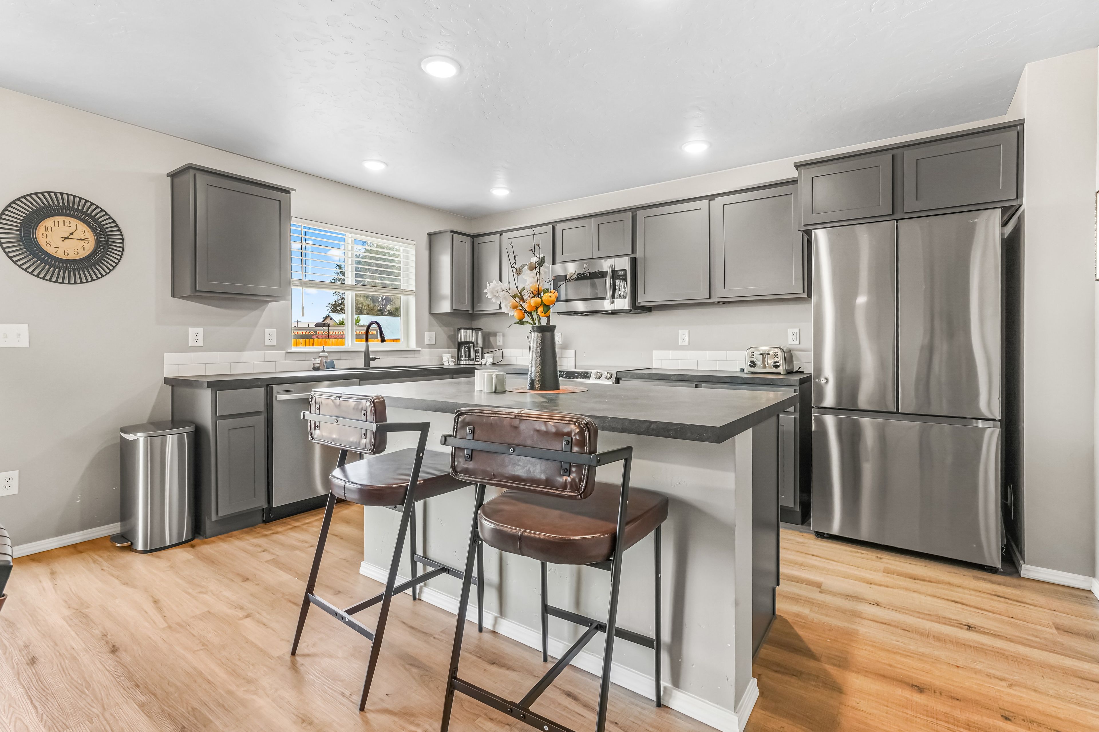 A modern kitchen with stainless steel appliances, a central island with bar stools, and a decorative clock on the wall.