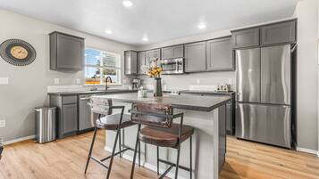 A modern kitchen with stainless steel appliances, a central island with bar stools, and a decorative clock on the wall.