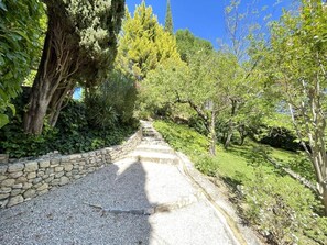 A gravel pathway flanked by stone walls and lush greenery, leading through a garden with various trees and shrubs. - Vacation Rental with Pool and Sauna (MONTFERRAT)