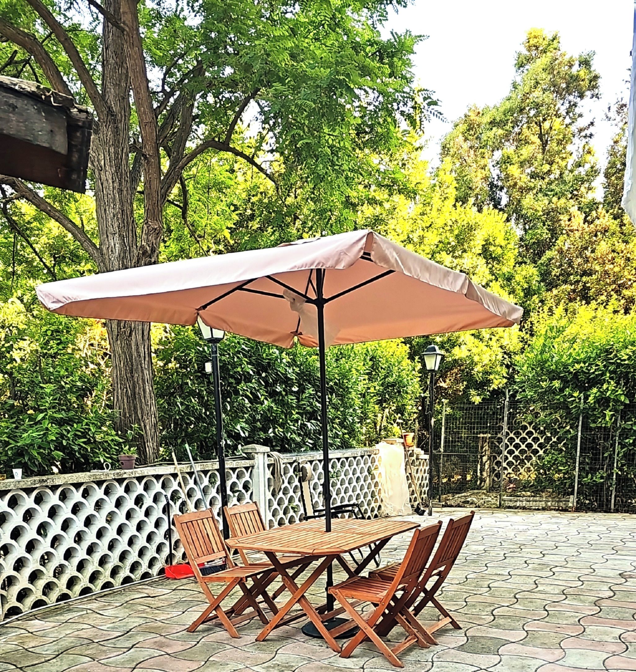 Une terrasse extérieure avec une table et des chaises en bois, un grand parasol et une clôture décorative.