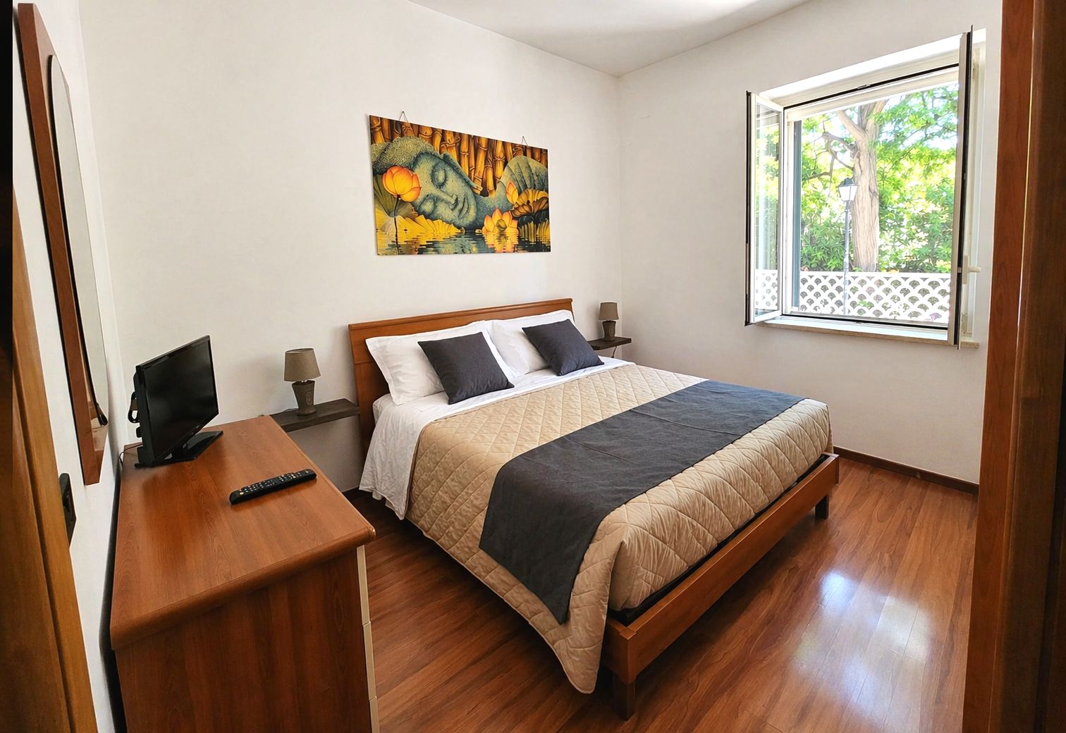 A bedroom with a bed, bedside tables, a TV, and a window.