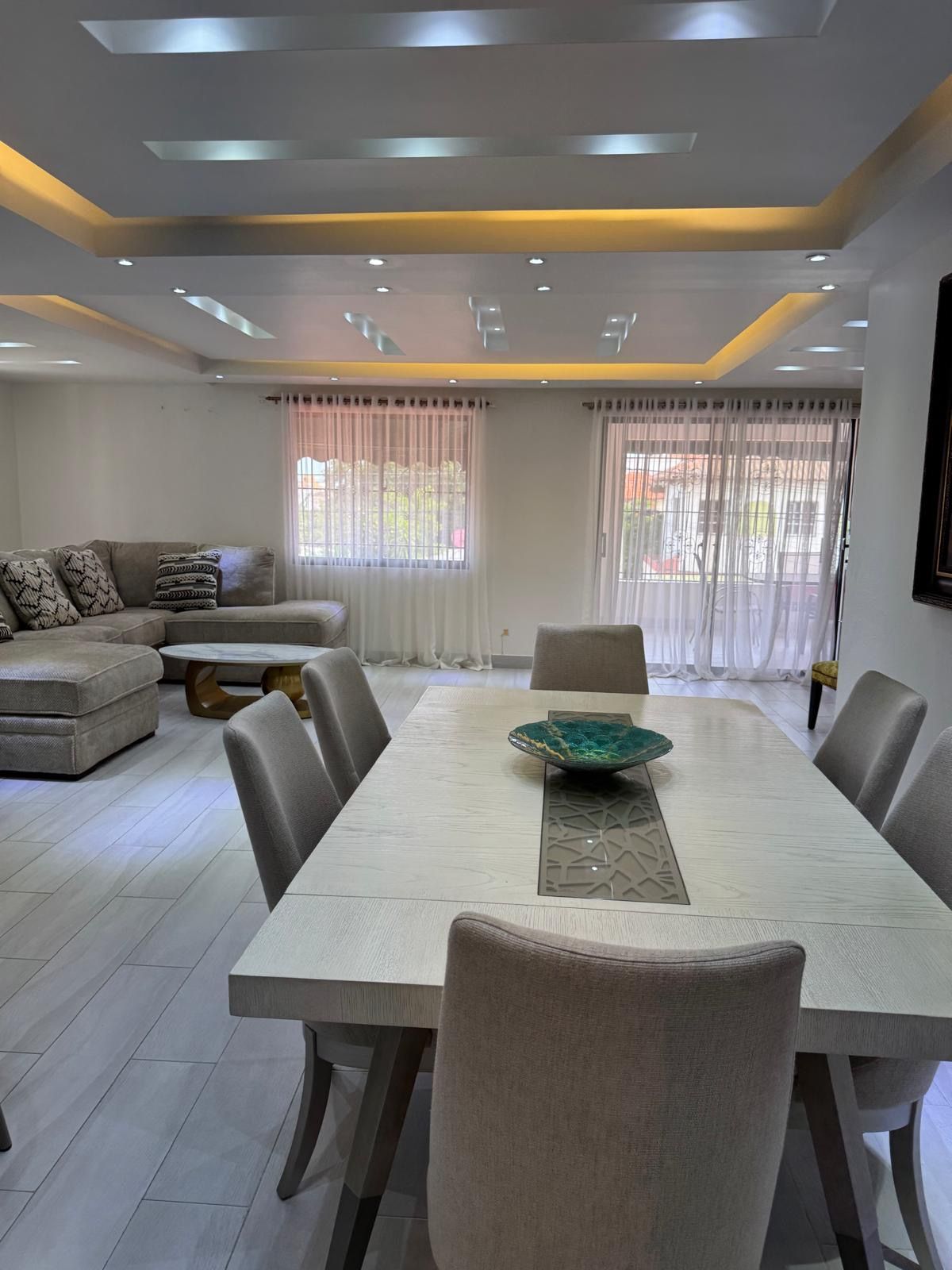 A modern dining area with a rectangular table, cushioned chairs, and a decorative bowl centerpiece.