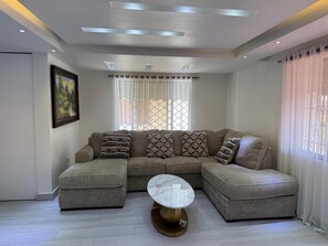 A modern living room with a sectional sofa, a round coffee table, and a painting on the wall. - Carolina Apartment (Los colonos)