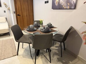 A dining area with a glass-top table, four chairs, and a vase with flowers.