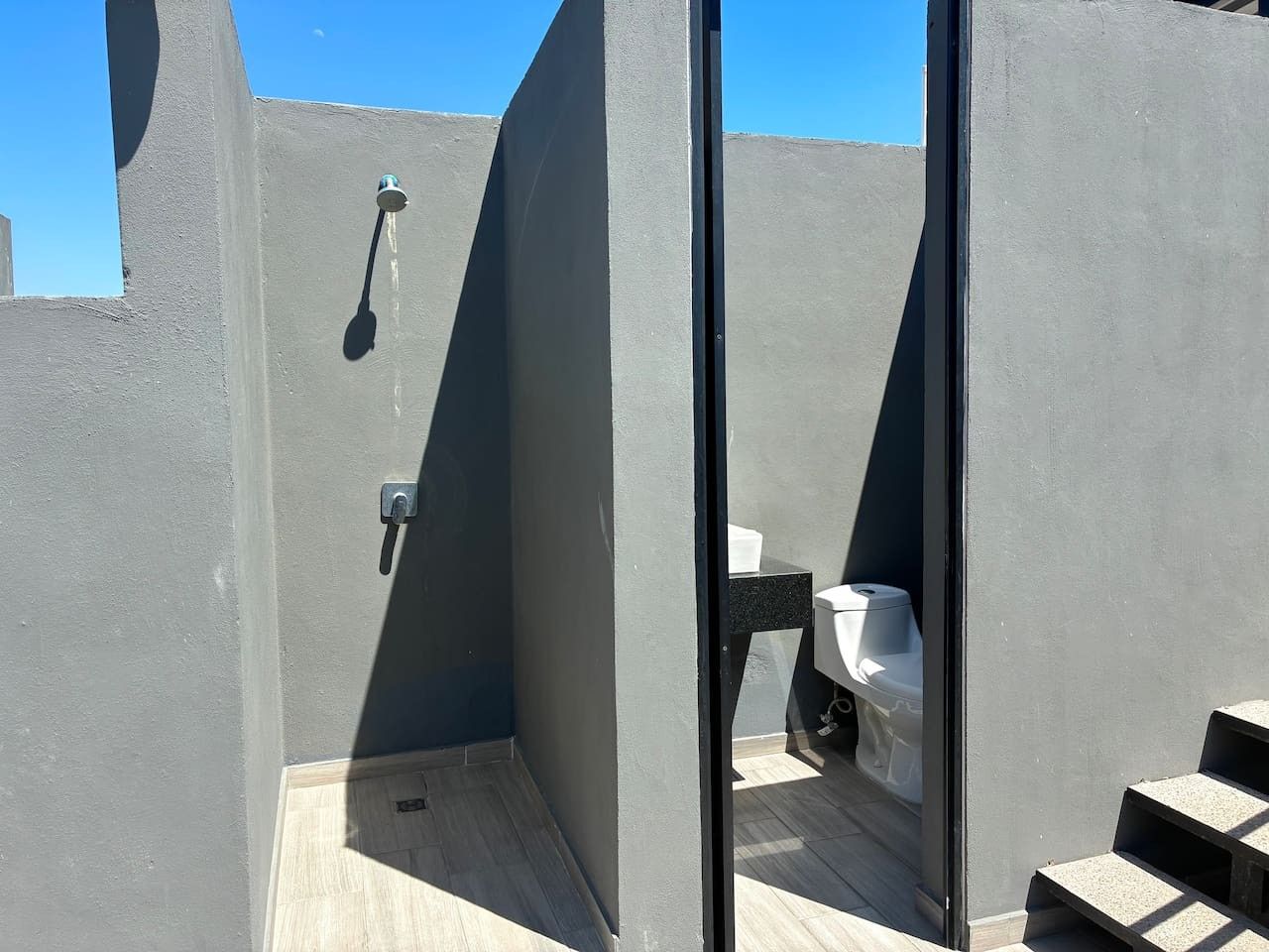A modern outdoor bathroom with a toilet and shower area, enclosed by a glass partition.