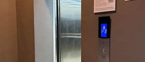 An elevator interior with a digital display showing 'P B' and a wall-mounted sign with safety instructions.
