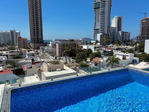 A rooftop swimming pool with a view of surrounding buildings and palm trees.