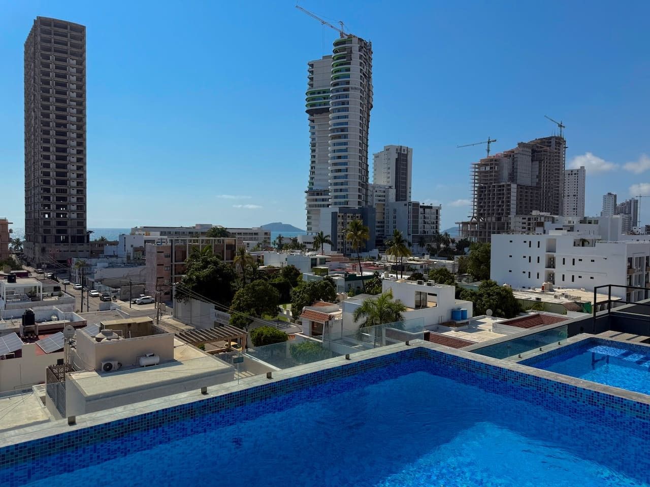 Une piscine sur le toit offrant une vue panoramique sur la ville, avec notamment des gratte-ciel et des grues de construction.
