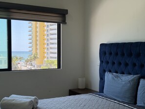 Ein Hotelzimmer mit großem Fenster, einem Bett mit einer gesteppten Kopfteil und einem Nachttisch mit einer Lampe.