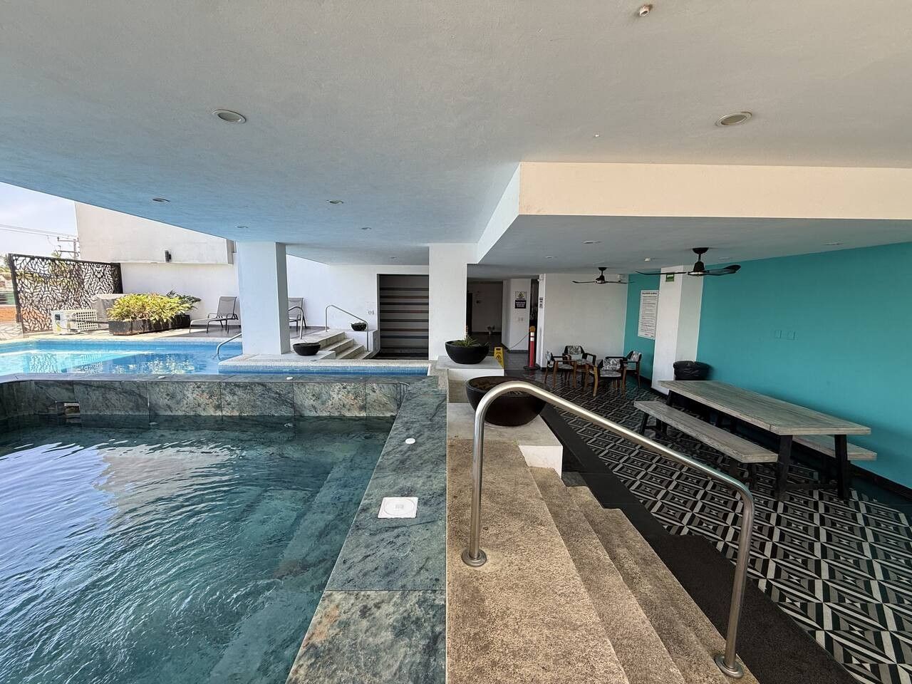 Un espace autour de la piscine offrant une vue dégagée sur celle-ci, un escalier menant à un niveau supérieur et un coin salon avec des tables et des chaises.