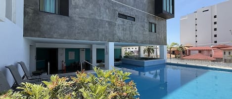 A modern building with a pool, outdoor seating, and a view of the surrounding area.