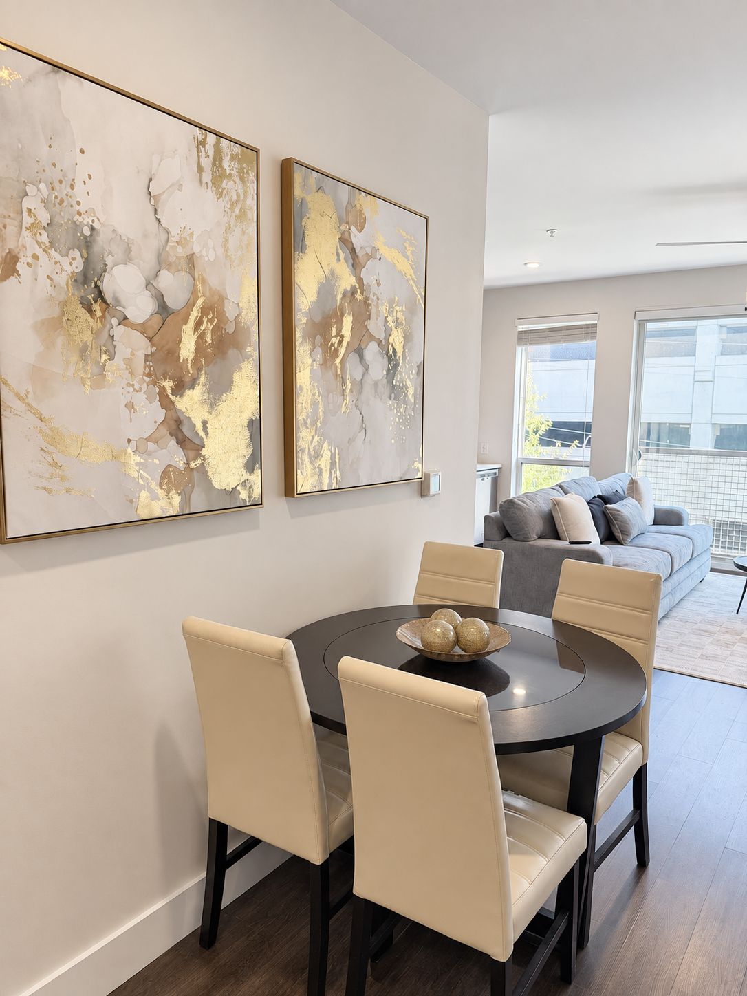 Een eetruimte met een ronde tafel, zes stoelen en twee abstracte schilderijen met gouden lijsten aan de muur.