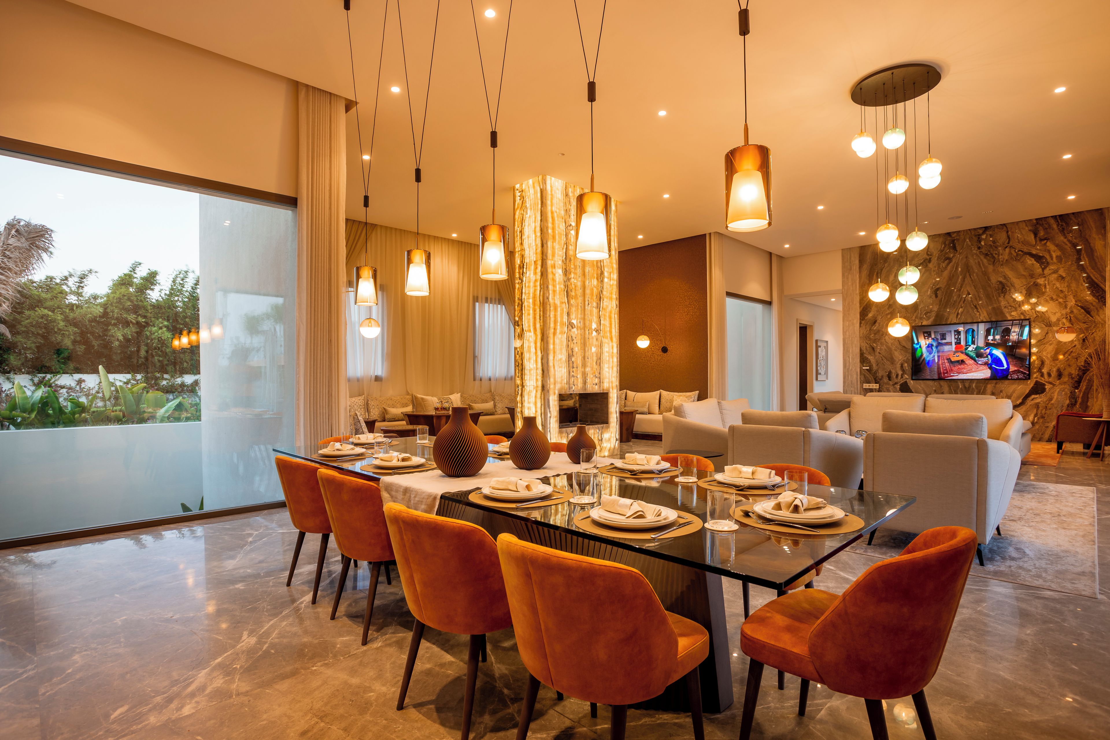Un comedor moderno con una mesa de vidrio, sillas naranjas e iluminación colgante.