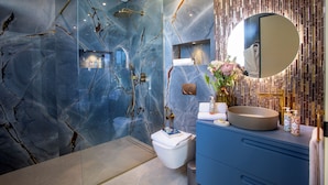 Un baño moderno con pared de mármol, ducha dorada y tocador azul.