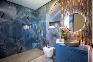 Une salle de bain moderne avec un mur en marbre, une douche dorée et un meuble-lavabo bleu.