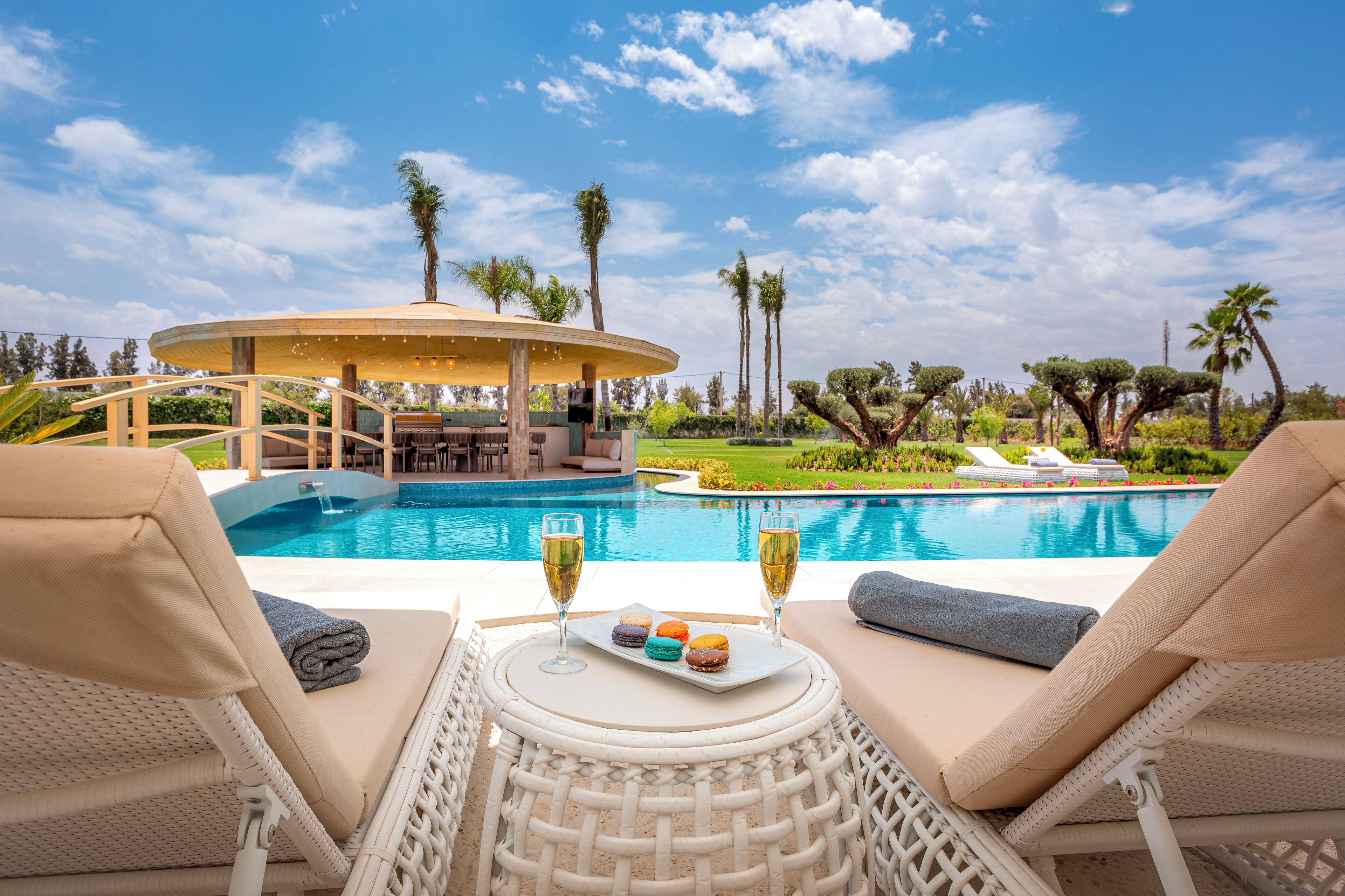 A poolside area with lounge chairs, a table with drinks and snacks, and a covered seating area with a view of the pool and surrounding landscape.