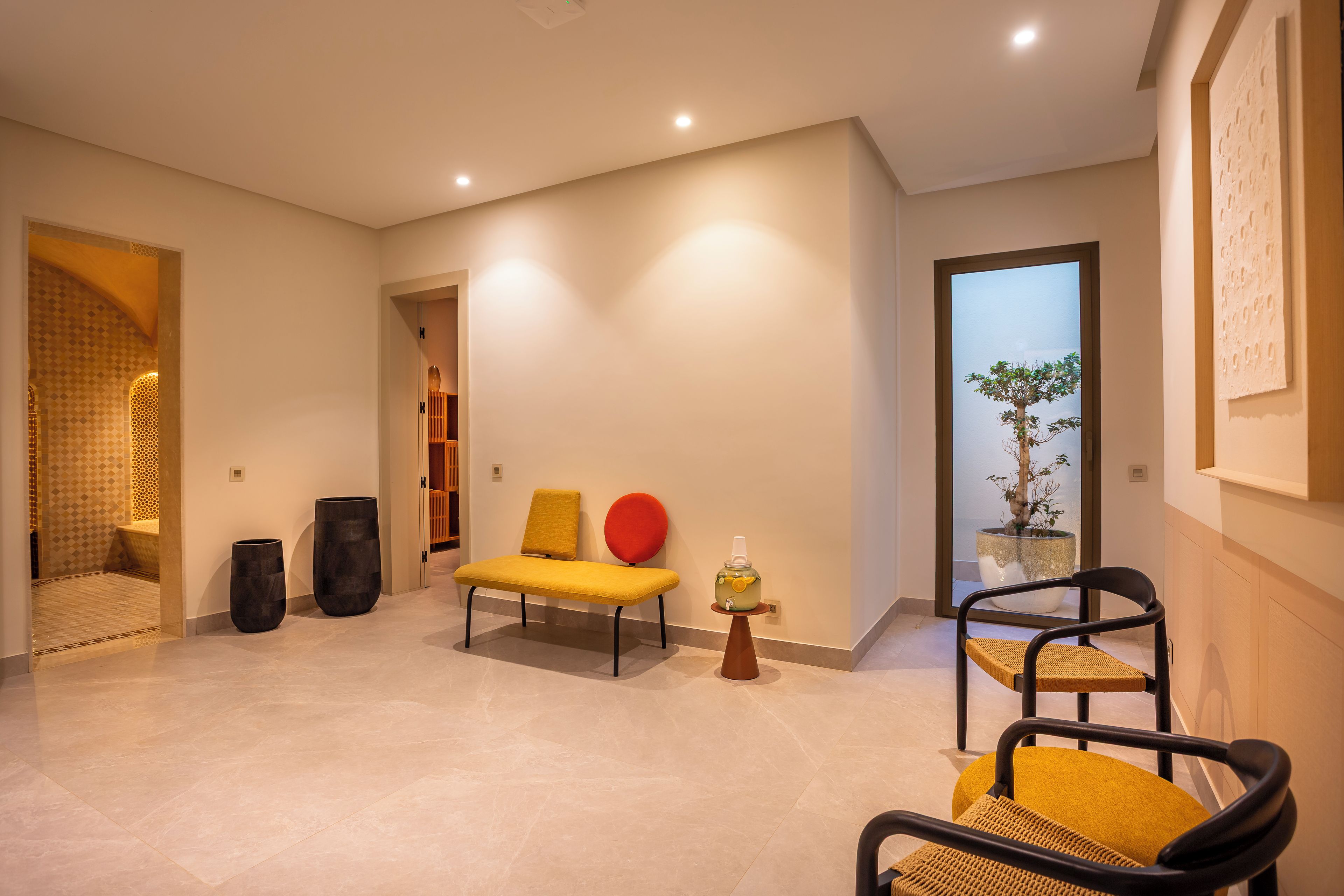 A modern living room with a sofa, chairs, a potted plant, and a decorative vase.