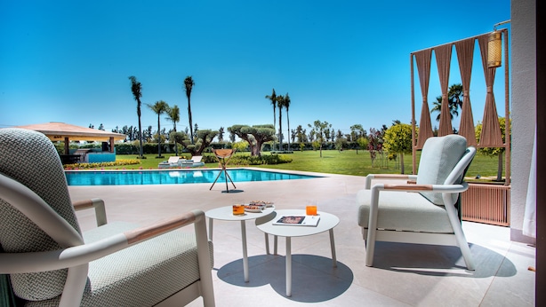 Zona junto a la piscina con dos sillas, una mesita y vistas a una piscina y jardín.