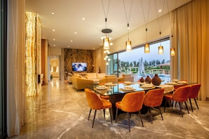 A modern dining area with a large table, orange chairs, and a television in the background. - Villa Olympus (Marrakech)