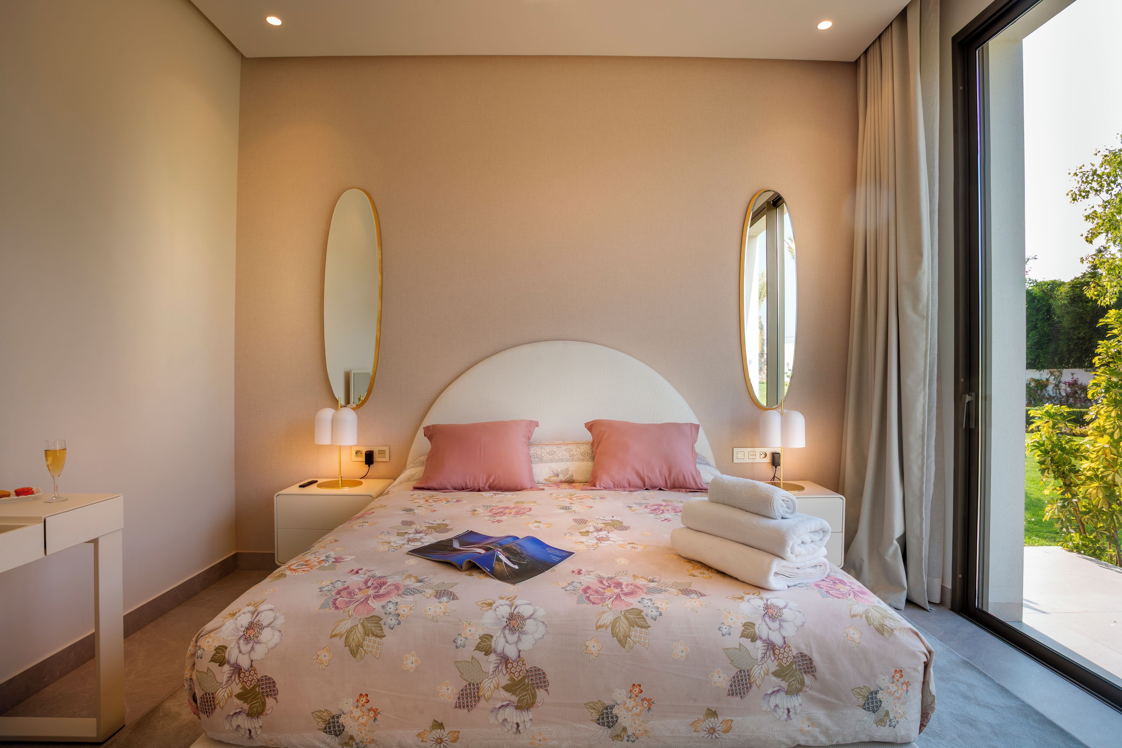 Ein Schlafzimmer mit einem großen Bett, zwei Nachttischen, einem Schminktisch und einem Fenster mit Vorhängen.