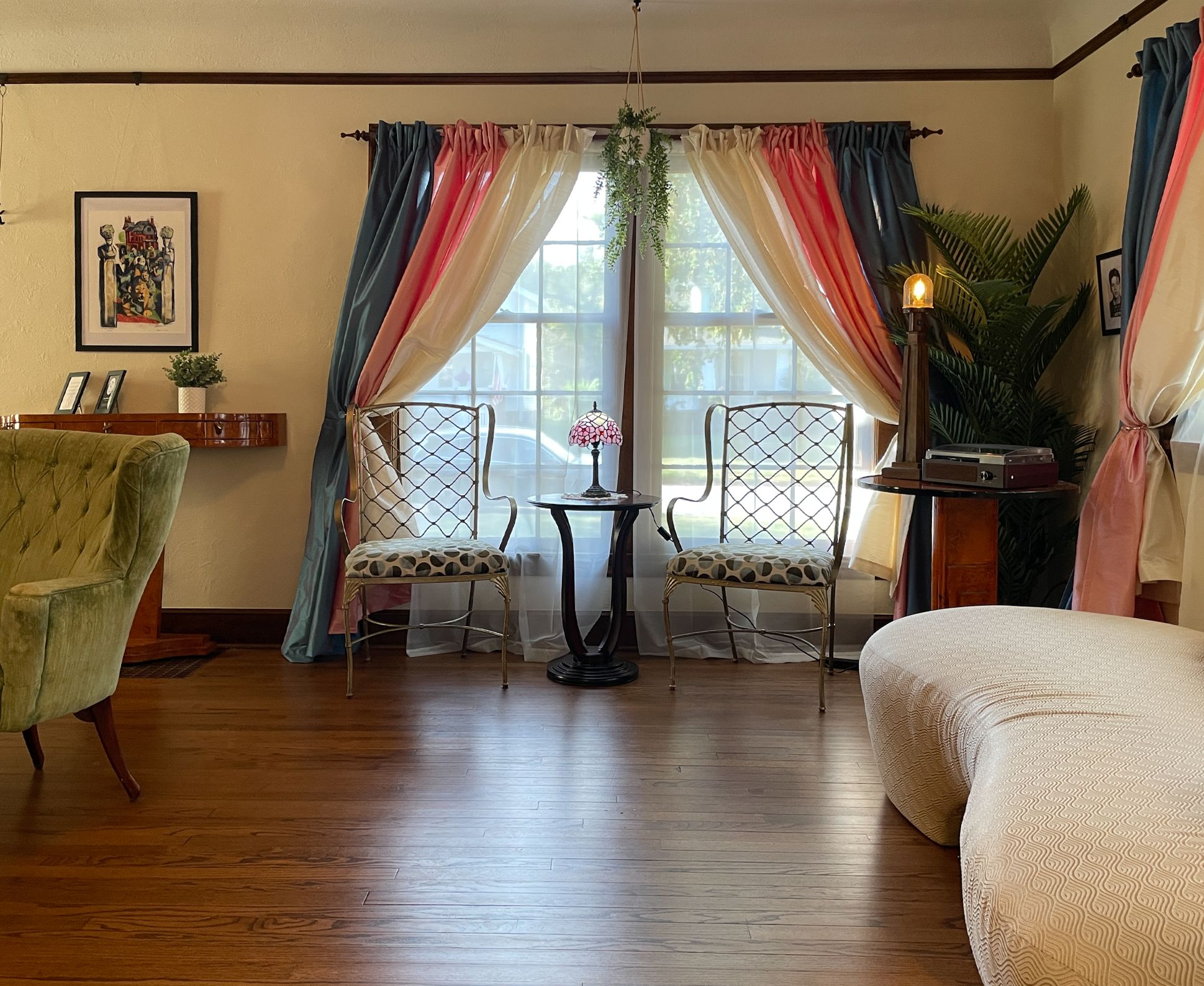 A room with a wooden floor, two chairs, a small table, a lamp, and a bed.