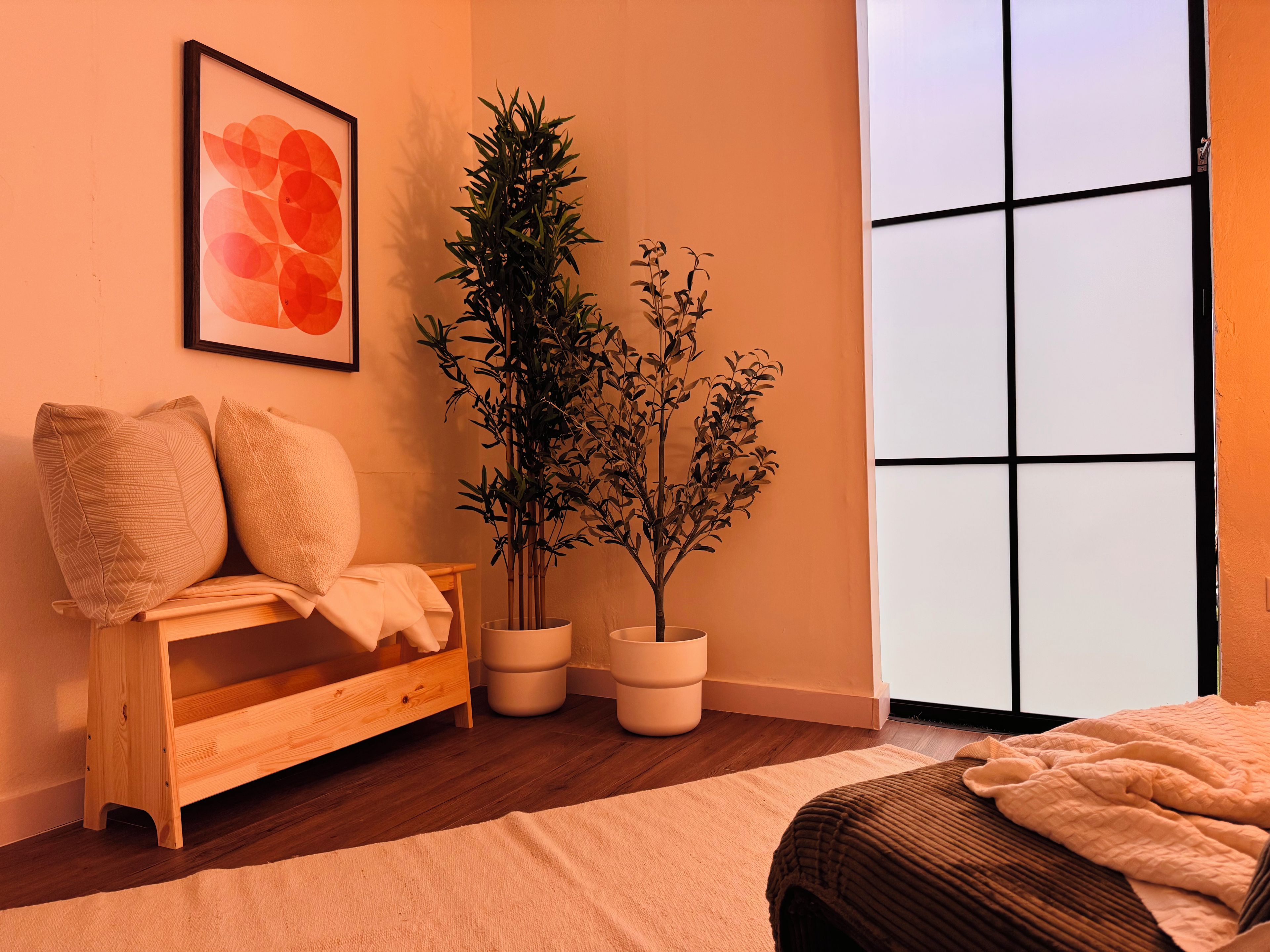 Una habitación con un banco de madera, una planta en maceta, una obra de arte enmarcada y un ventanal grande.