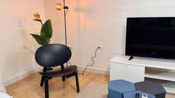 Een moderne woonkamer met een flatscreen televisie, een zwarte stoel, een plant in pot en een vloerlamp.