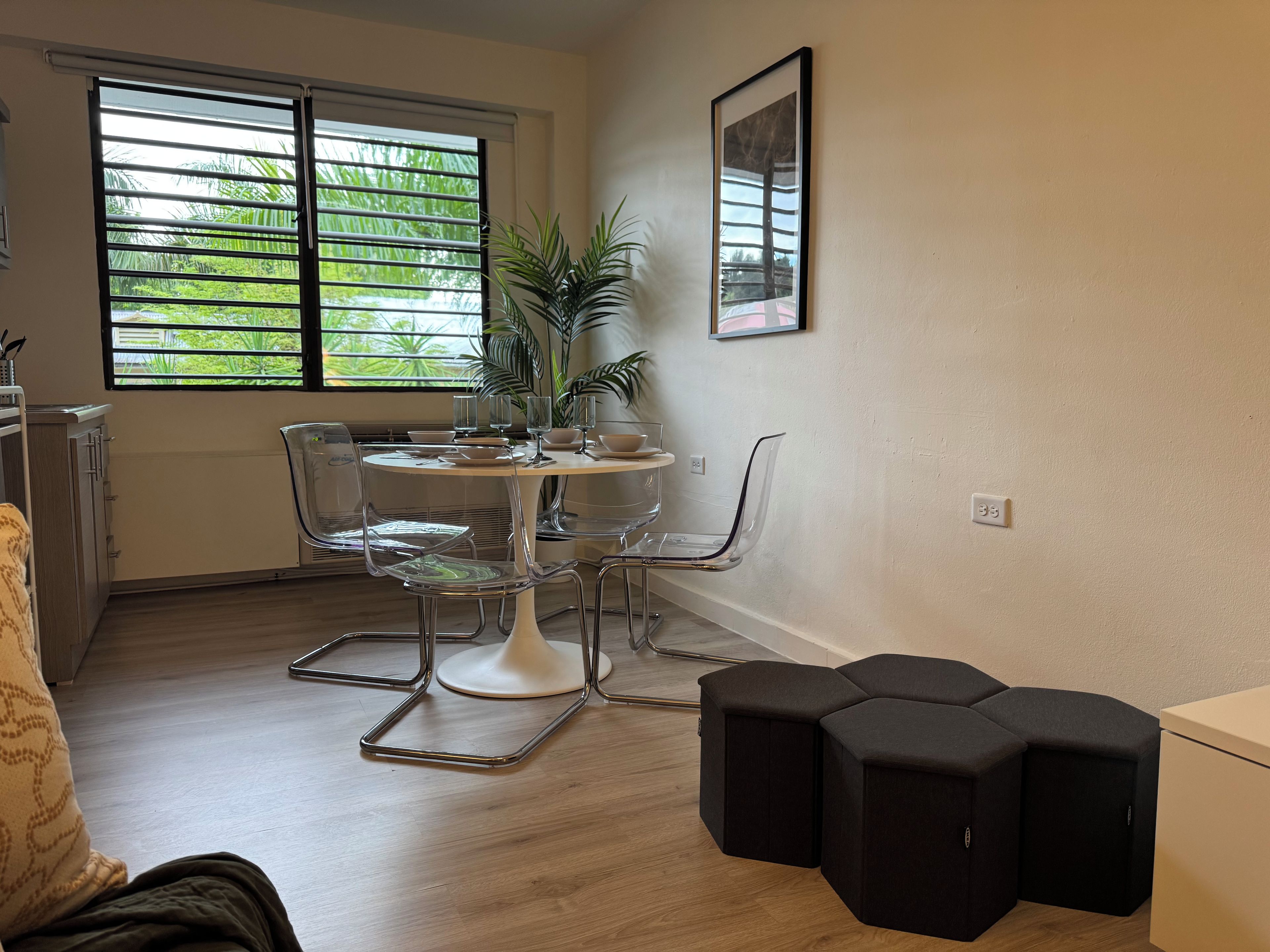 Un comedor con una mesa redonda, sillas transparentes y una planta en maceta.