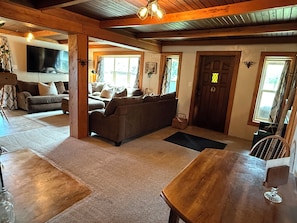 A cozy living room with a sofa, wooden dining table, and a TV mounted on the wall.