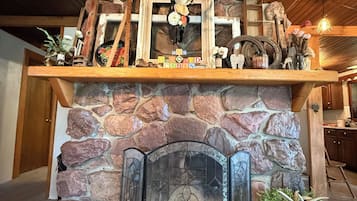 Una chimenea de piedra con una puerta de vitral, un fuste de madera adornado con astas y flores, y una pequeña mesa con plantas.