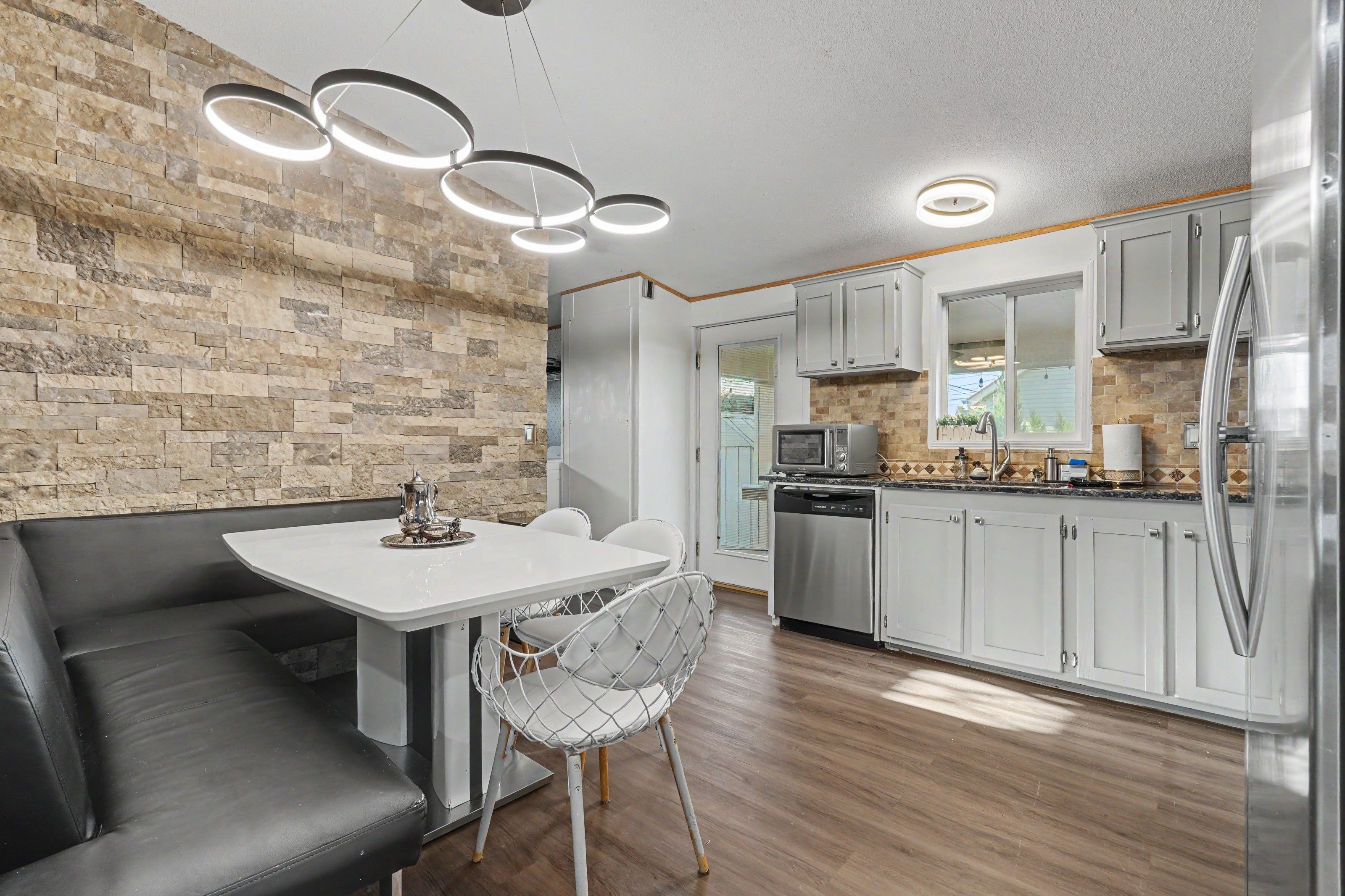 A modern kitchen with a stone wall, a dining area with a white table and chairs, and a built-in oven.