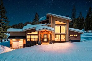 A modern multi-story house with a snow-covered roof, large windows, and a well-lit entrance. - McCall 4BR House • Fireplace • Near Brundage (McCall)