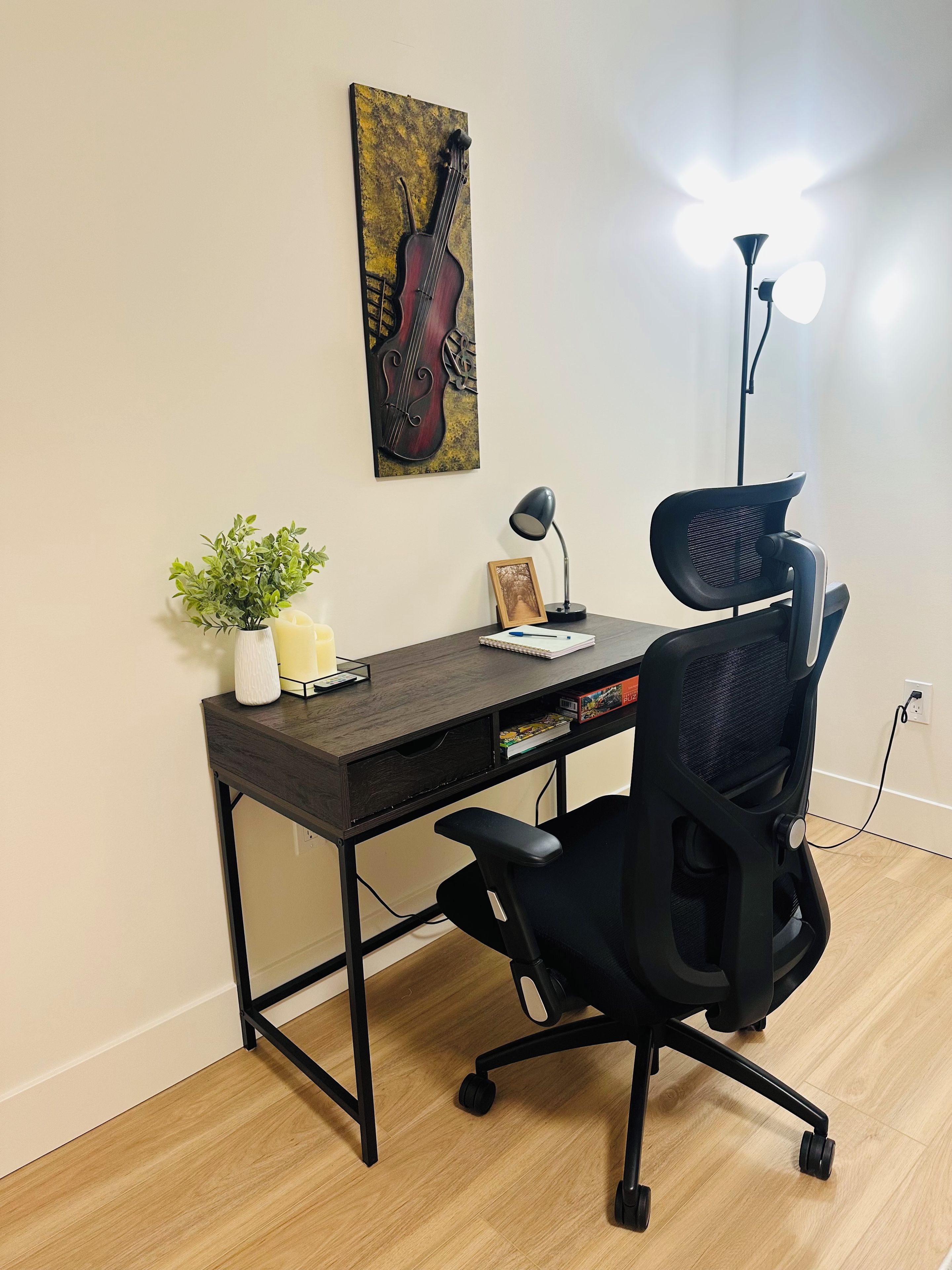 A workspace with a desk, chair, lamp, and a wall-mounted picture of a cello.