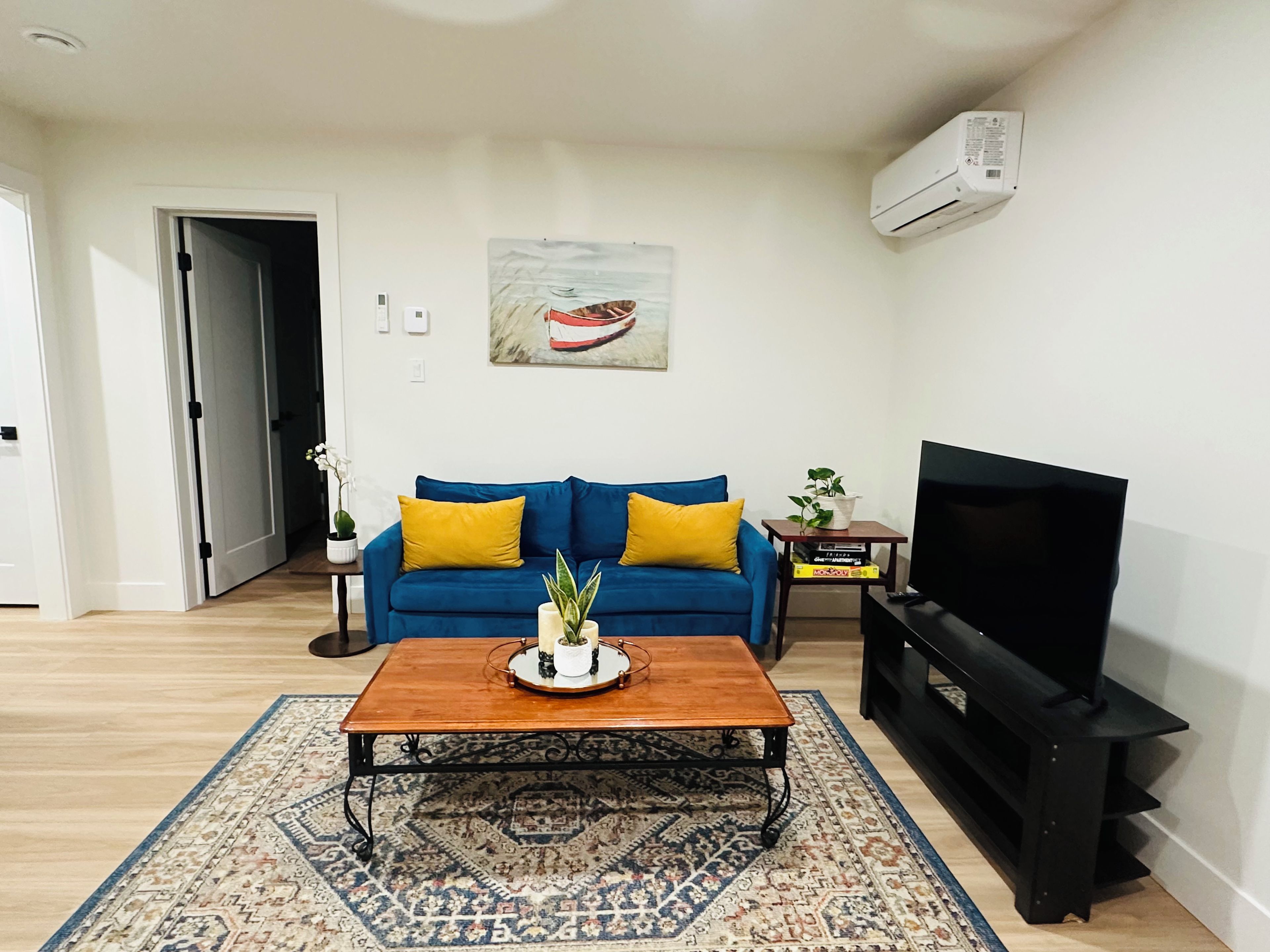 A living room with a blue sofa, a coffee table, a TV stand, and a patterned rug.