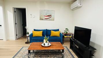 A living room with a blue sofa, a coffee table, a TV stand, and a patterned rug.