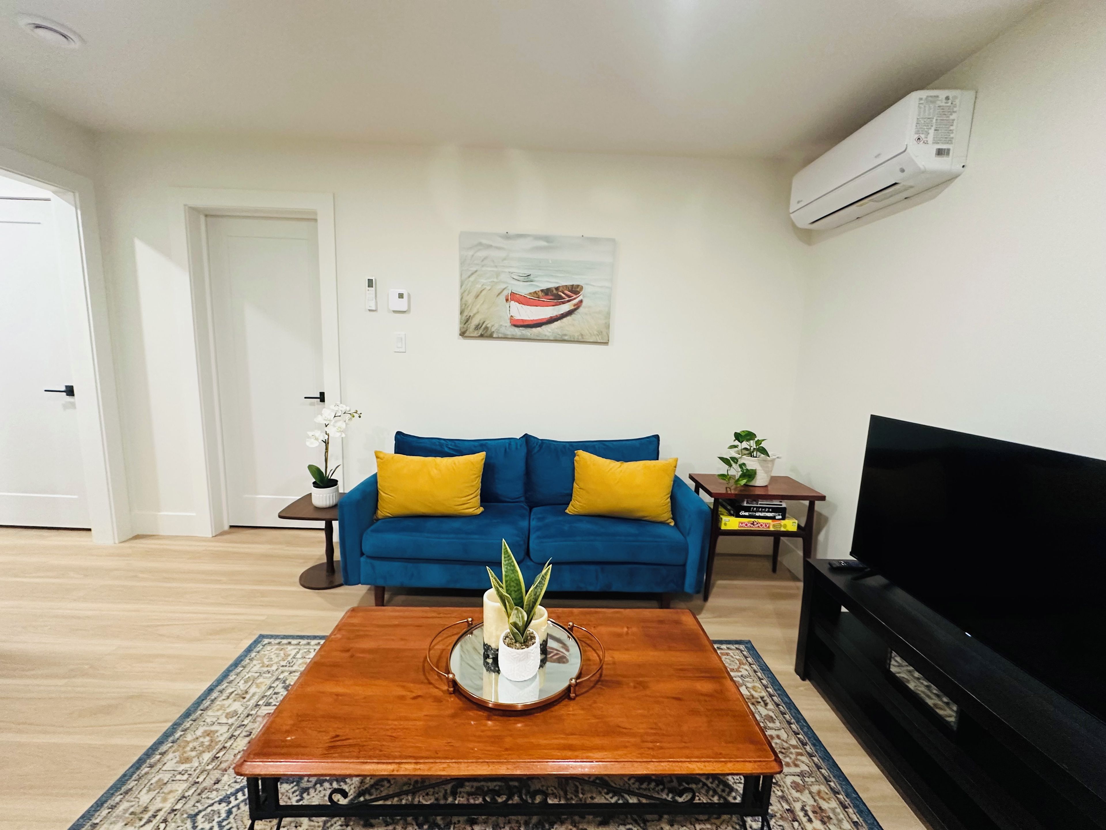 A living room with a blue sofa, a coffee table with a plant, a flat-screen TV, and a painting on the wall.