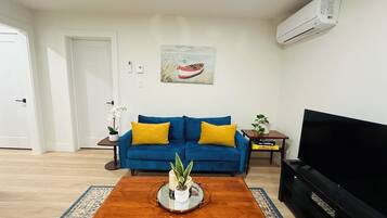 A living room with a blue sofa, a coffee table with a plant, a flat-screen TV, and a painting on the wall.