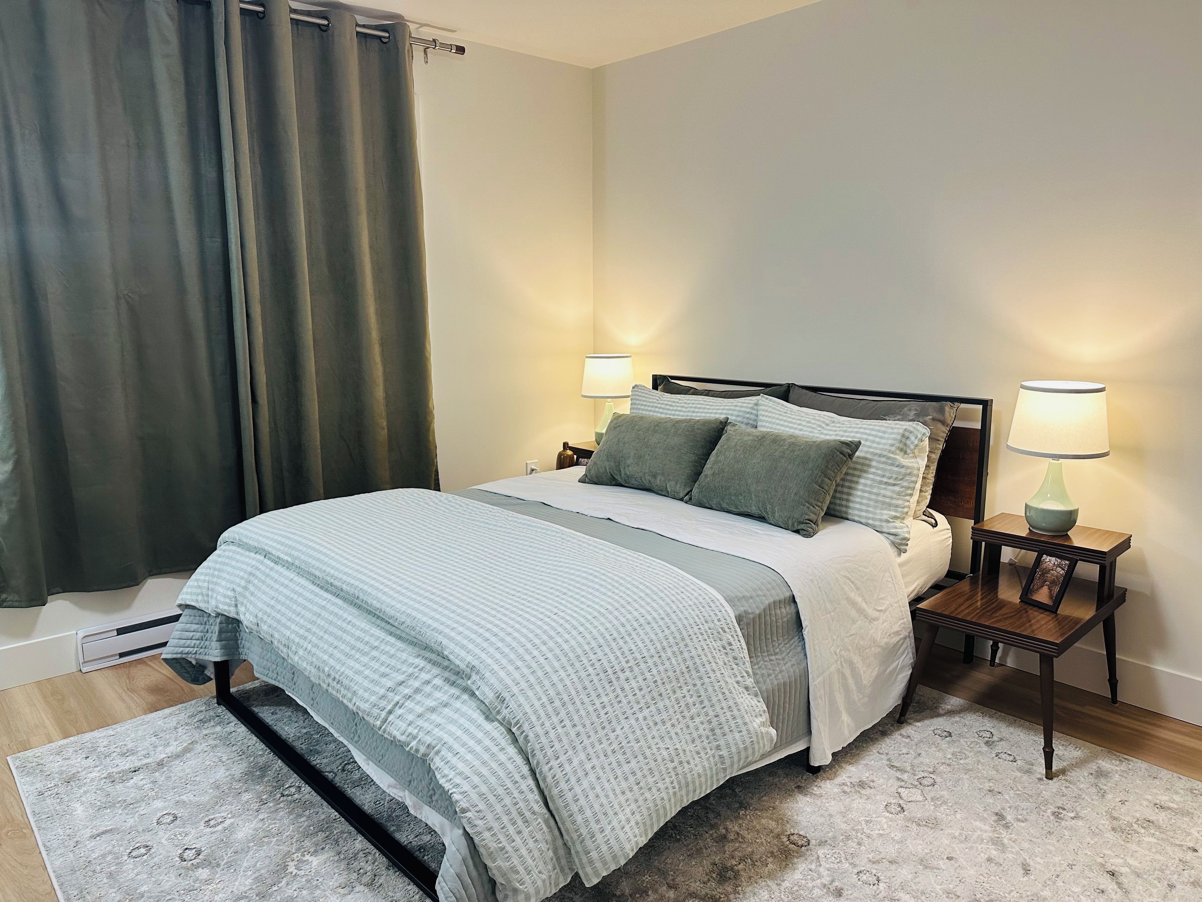 A neatly made bed with a striped bedspread, two bedside lamps, and a small bedside table with a picture frame.