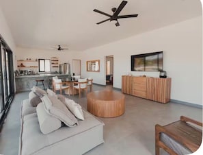 A spacious living area with a sofa, a round wooden coffee table, a TV, and a ceiling fan. - Villa with Sauna. Villa Serena (Todos Santos)