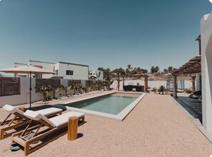 A modern outdoor pool area with lounge chairs, a pergola, and a view of the surrounding buildings. - Villa with Sauna. Villa Serena (Todos Santos)