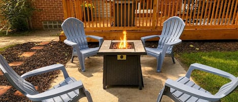 A patio with a fire pit and four Adirondack chairs.