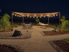 Ein Sitzbereich im Freien mit Tisch, Stühlen, einer Hängematte und Lichterketten.