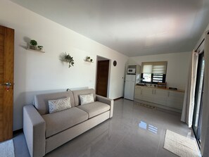 A modern living room with a sofa, a kitchen area with a microwave and refrigerator, and a door leading to another room.