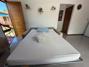 A bedroom with a bed, pillows, a wall clock, and two shelves with plants. - FARE HANI - Combining comfort and privacy with a pool (Maatea)