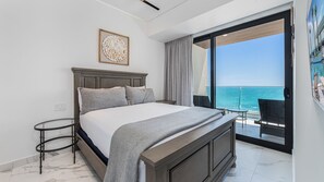 Ein Schlafzimmer mit einem Bett, einem kleinen Tisch, einem Gemälde und Blick auf den Ozean durch eine Schiebetür.