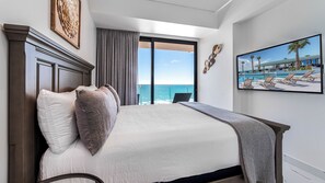 A hotel room with a large bed, a view of the ocean, a painting of a pool, and a wooden headboard. - Elegant 3BR Condo with Breathtaking Ocean Views (Puerto Peñasco)