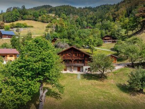 Eine Holzhütte mit Balkon, umgeben von üppiger Vegetation und weiteren Hütten in einer hügeligen Landschaft.