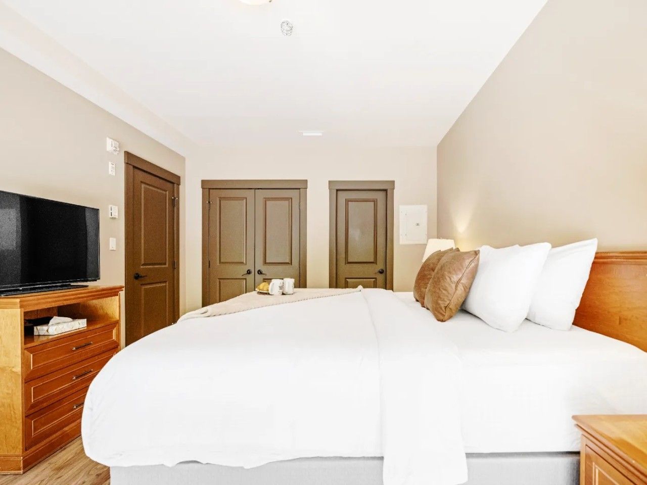 A hotel room with a large bed, wooden wardrobe, a flat-screen TV, and two doors.