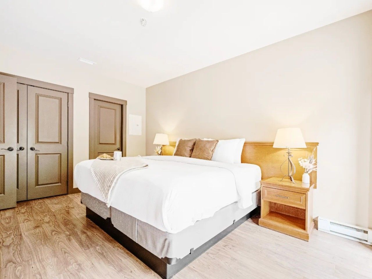 A bedroom with a bed, two bedside tables, a nightstand, and a door.