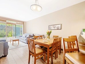 A dining area with a wooden table and chairs, a sofa, and a large window with a view.